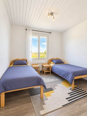 A bedroom with two single beds, a window with curtains, a small table, and a ceiling light fixture. - La Lagune - Bright House with Garden in Les Sables-d'Olonne (Les Sables-d'Olonne)
