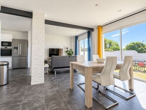 A modern kitchen with a built-in oven and microwave, a dining area with a wooden table and chairs, and a living area with a sofa and TV. - La Lagune - Bright House with Garden in Les Sables-d'Olonne (Les Sables-d'Olonne)