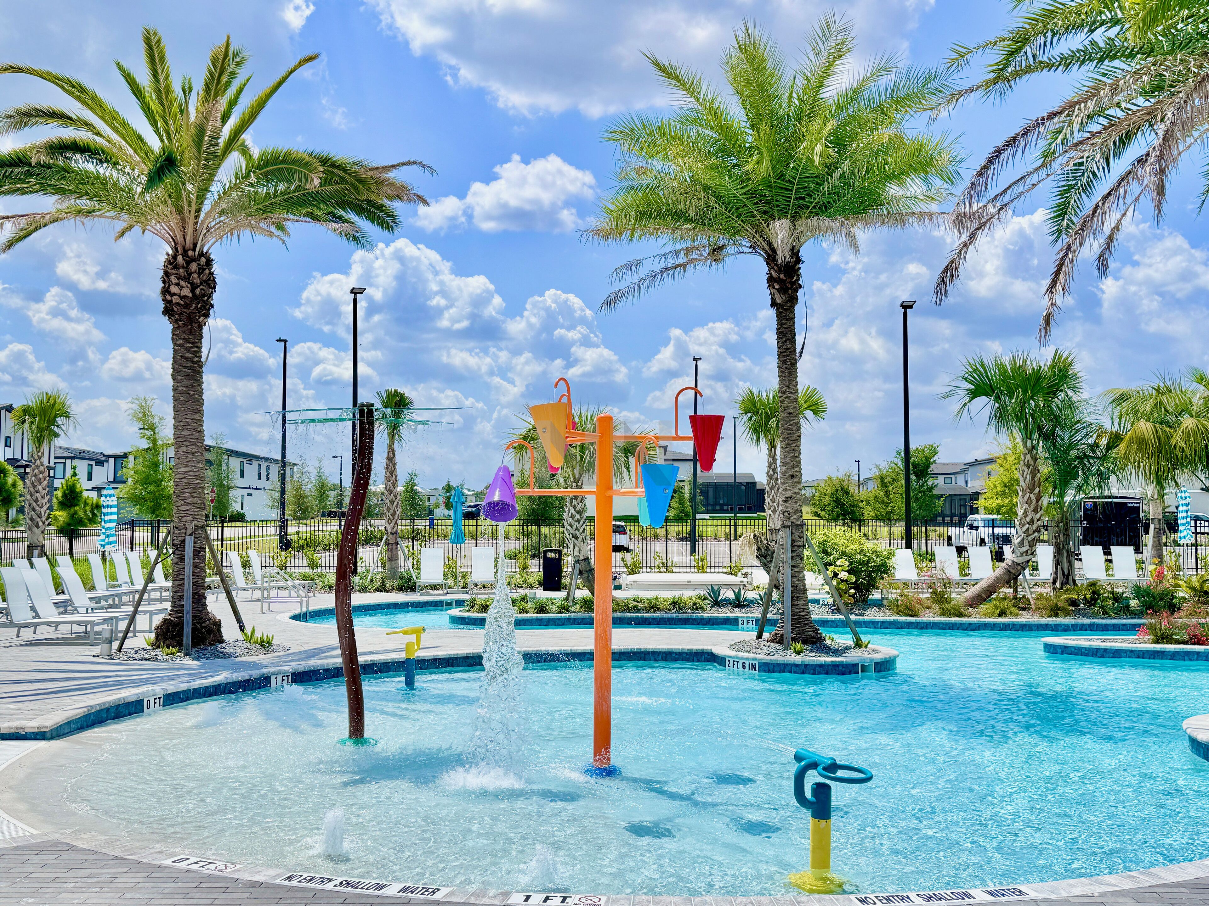 A swimming pool with water features, palm trees, and lounge chairs.