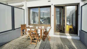 An outdoor seating area with a table and chairs, a sliding glass door, and a view of the street.