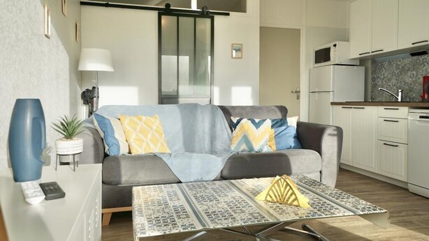 A modern living room with a sofa, a coffee table, and a kitchen area with cabinets and appliances.