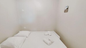 A single bed with white bedding and two rolled towels.