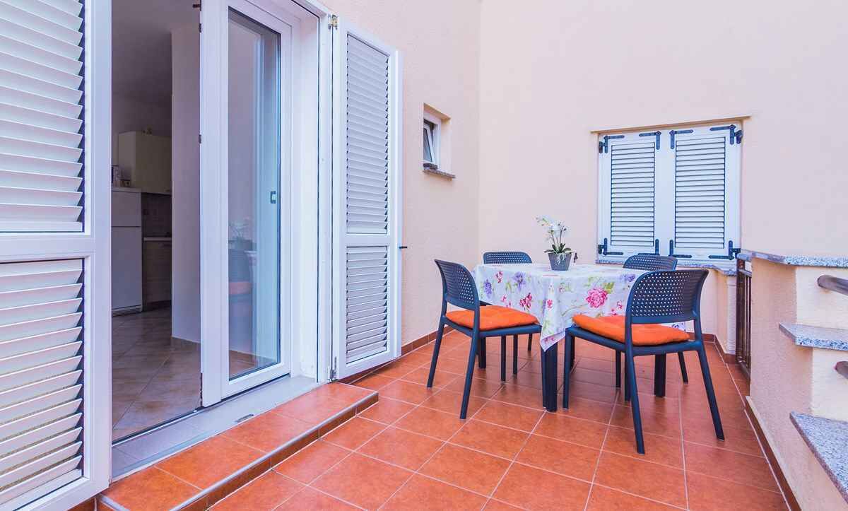 An outdoor patio with a table and chairs, a sliding glass door, and a small kitchen area visible through the door.