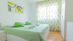 A bedroom with a bed, green pillows, a white nightstand, and a wall-mounted abstract art piece. - Holiday apartment with air conditioning (Pula)