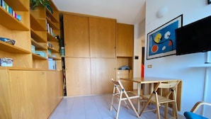 A compact kitchen with wooden cabinets, a dining table with chairs, and a blue chair. - Fornari 48 Comfortable Flat (Milan)
