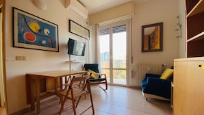 A living room with a wooden table and chairs, a blue sofa, and a TV on the wall. - Fornari 48 Comfortable Flat (Milan)