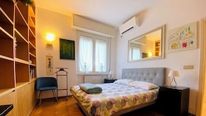 A bedroom with a bed, a chair, a wardrobe, a window, and a mirror. - Fornari 48 Comfortable Flat (Milan)