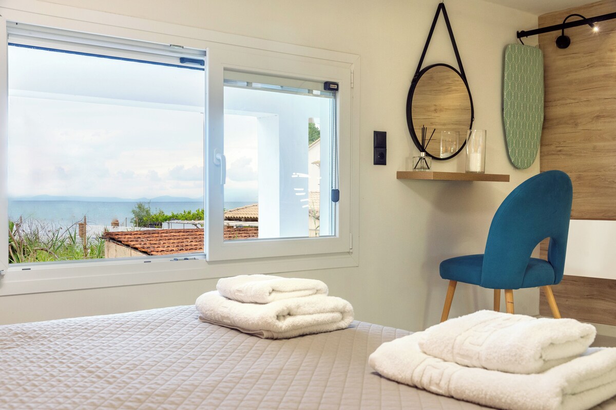 A bedroom with a large window, a blue chair, and neatly folded white towels on the bed.