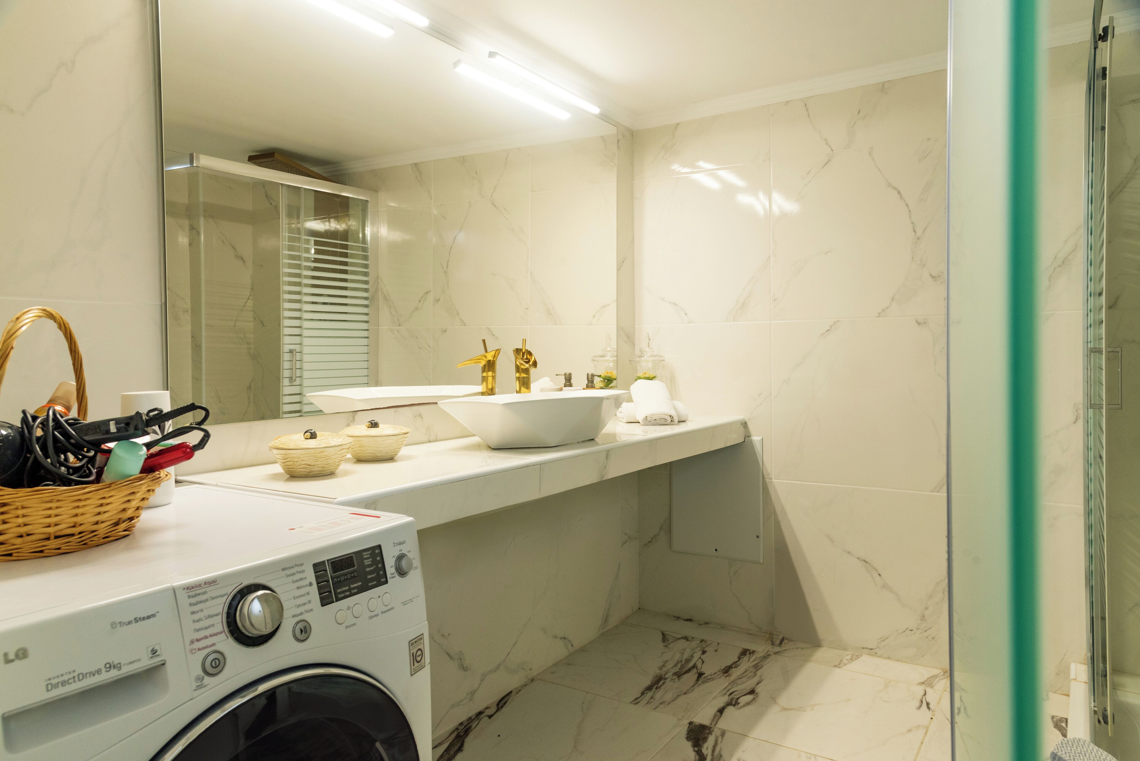 Un baño moderno con lavadora, un lavabo con detalles dorados y piso de mármol.