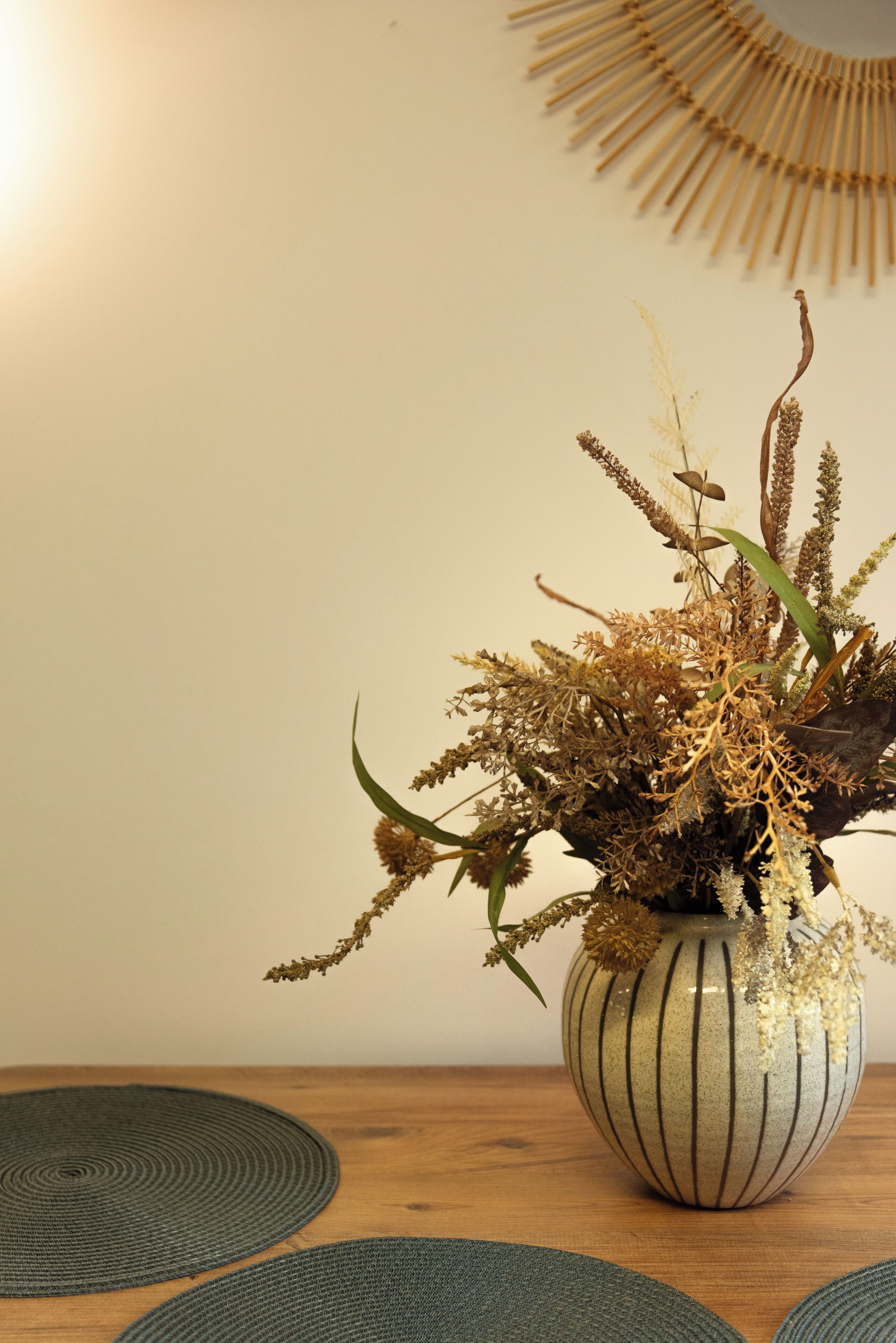 A vase with dried plants on a wooden table.