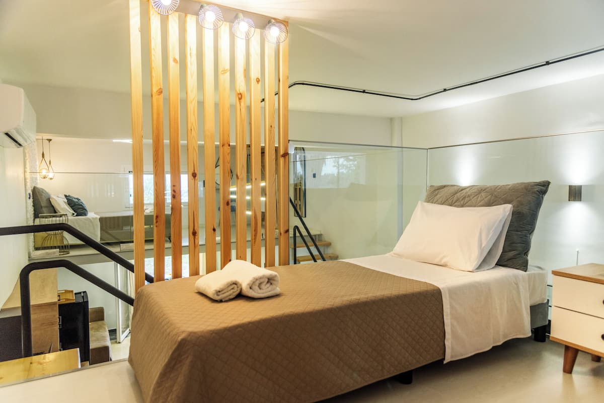 A modern hotel room with a bed, a nightstand, a wooden partition, and a staircase.