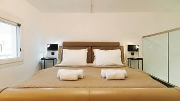 A neatly made bed with a brown headboard, two bedside tables with lamps, and a window with blinds.