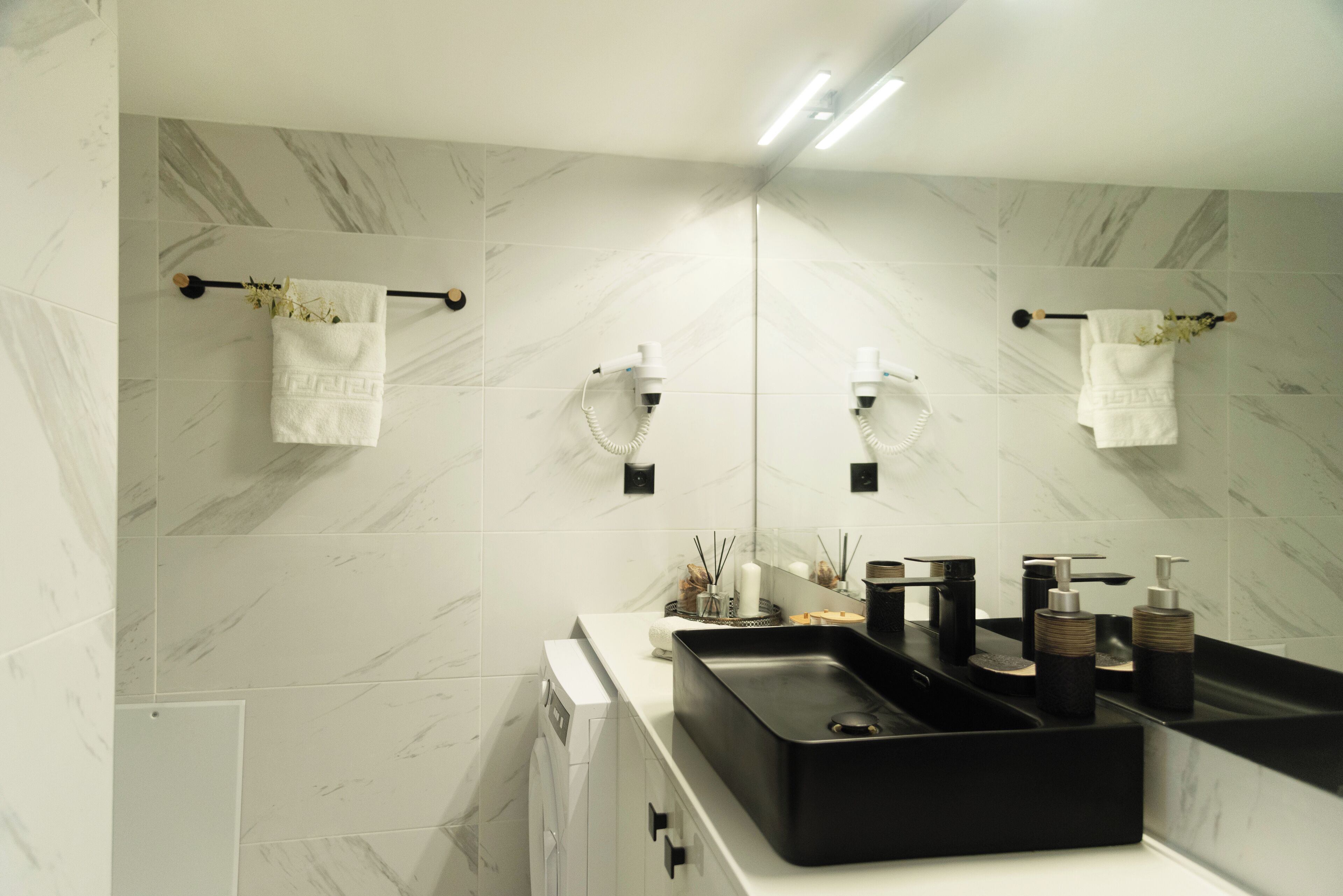 Un baño moderno con un lavabo negro, baldosas de mármol blanco y un espejo grande.
