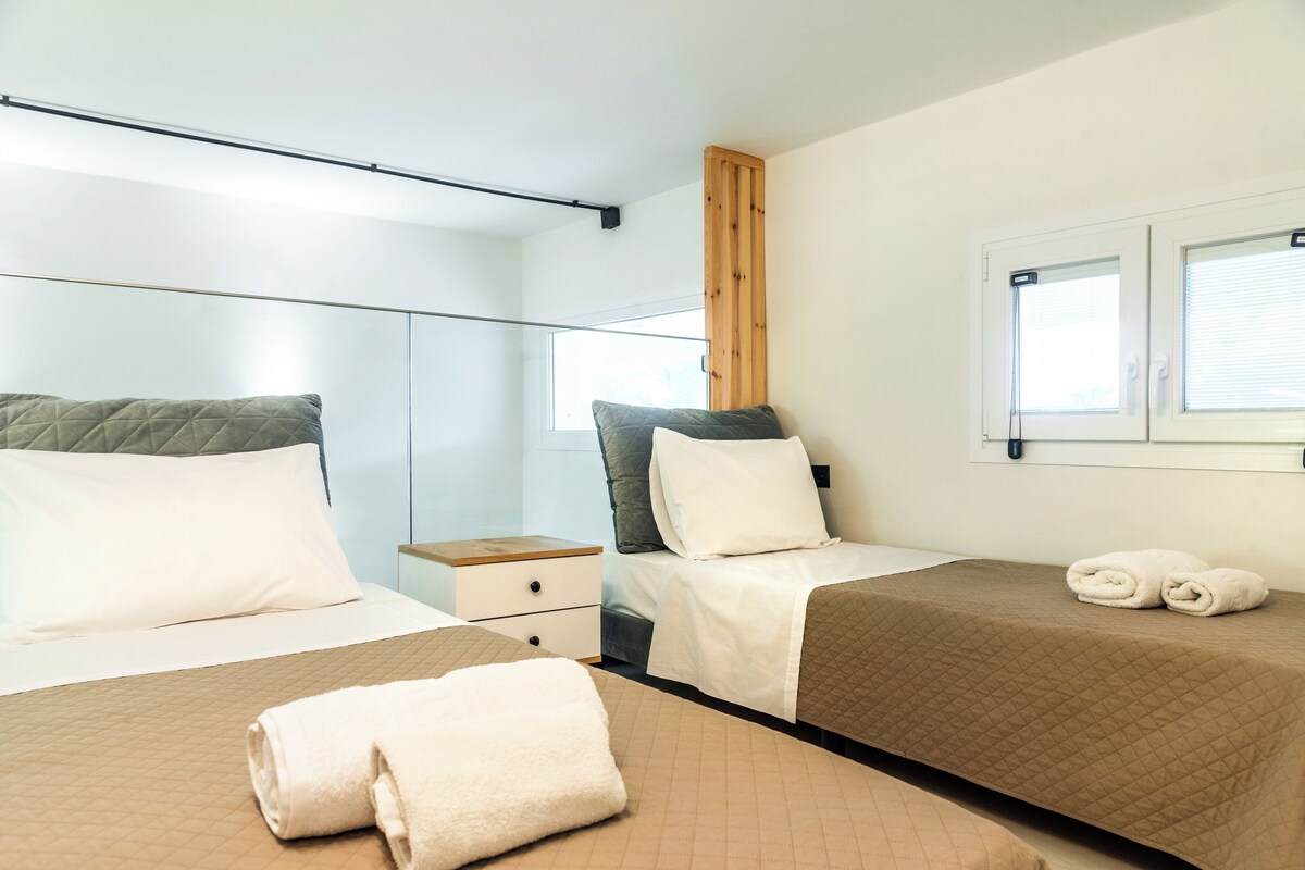 Habitación de hotel con dos camas, cabecero de madera, mesita de noche y ventana con persianas.