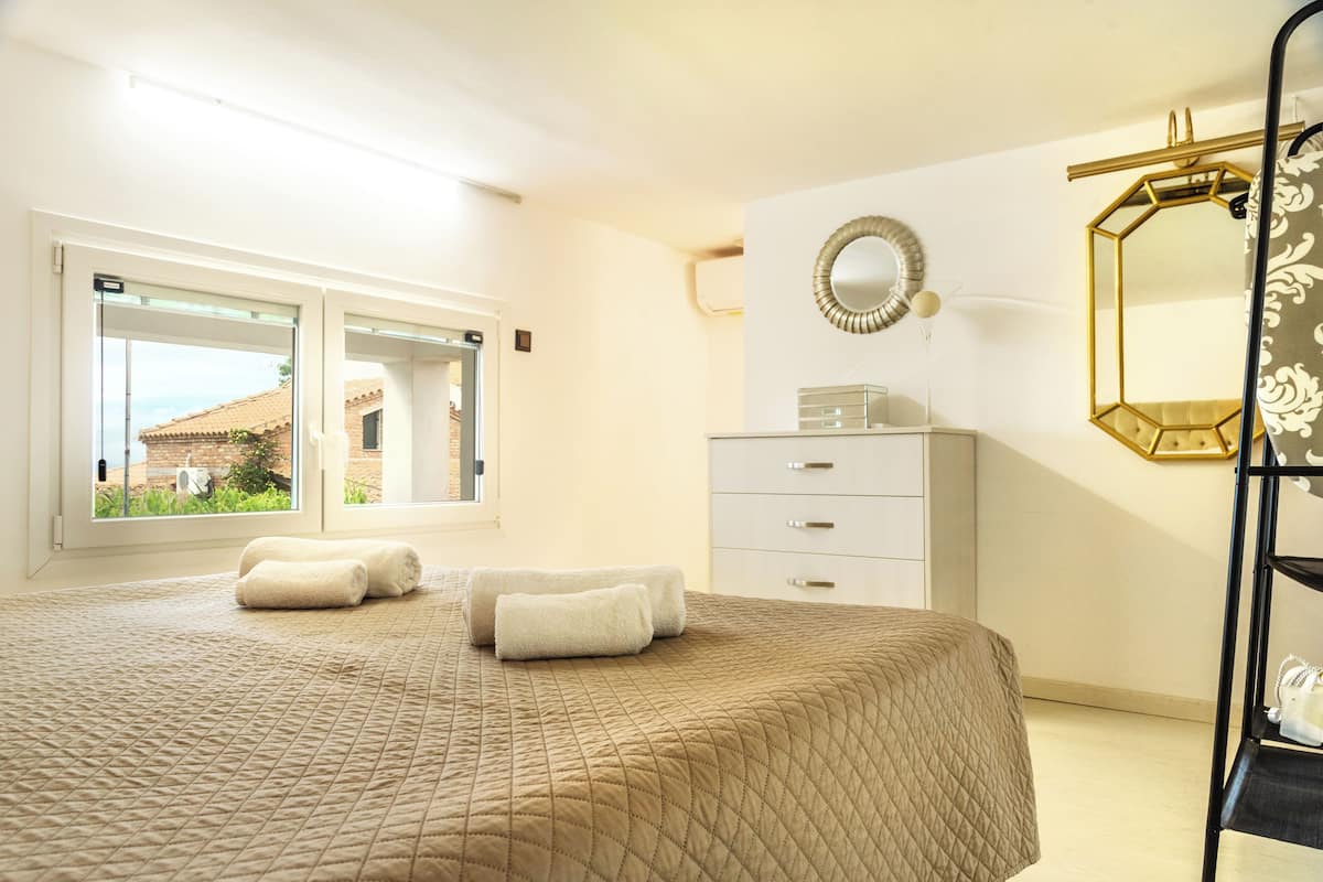 A hotel room with a large bed, a dresser, a mirror, and a window with a view of buildings.