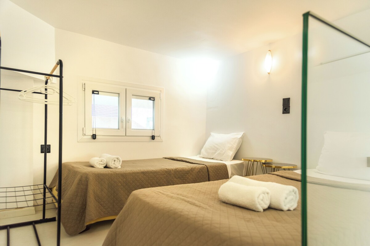 Una habitación de hotel con dos camas, una ventana con persianas, un perchero y una mesita.