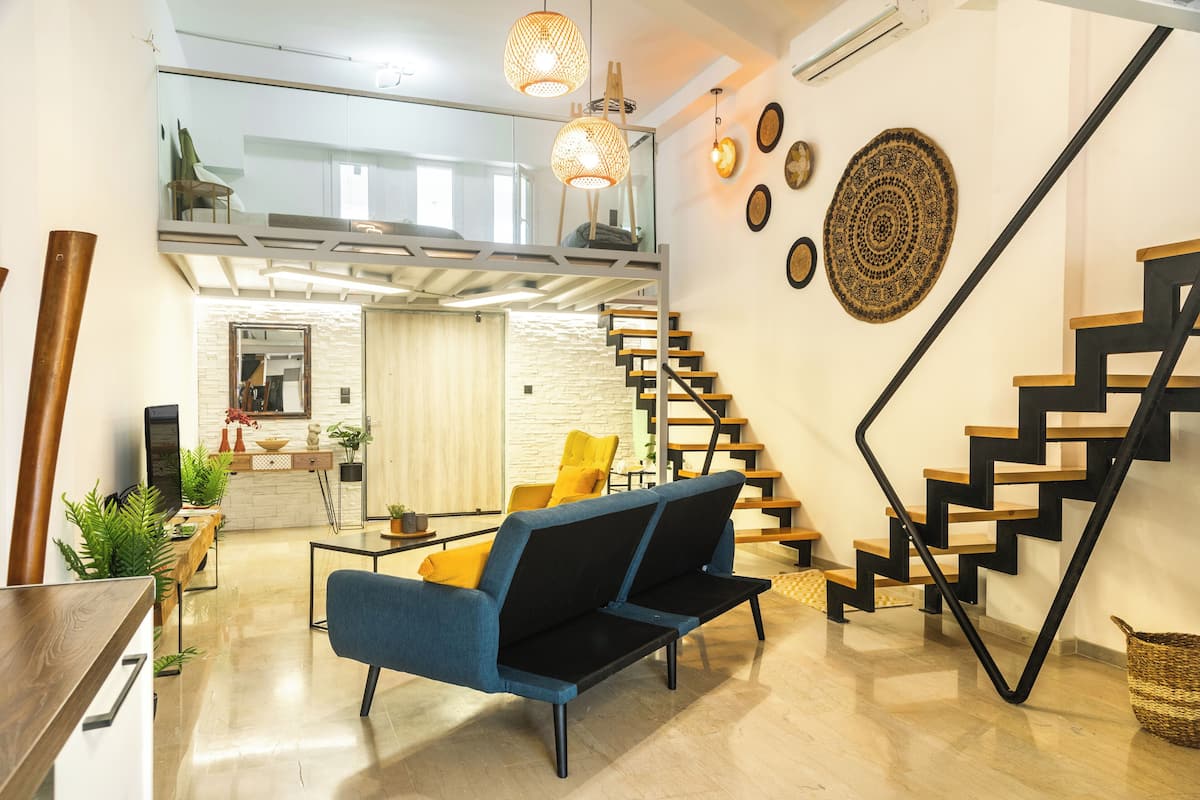 A modern living room with a sofa, a dining area, and a staircase.