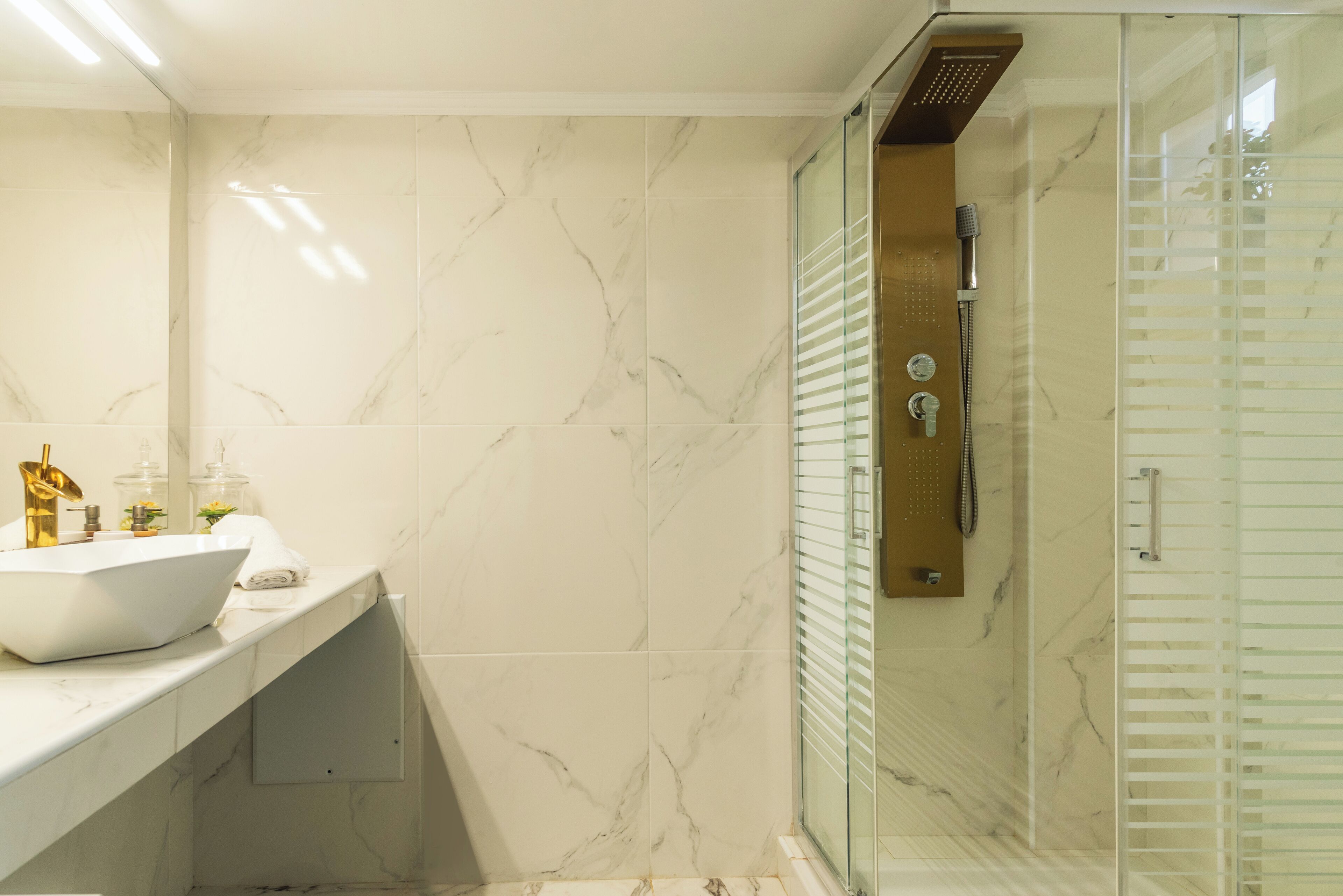 Ein modernes Badezimmer mit einem weißen Waschbecken, Marmorfliesen und einer Dusche mit Glastrennwand.