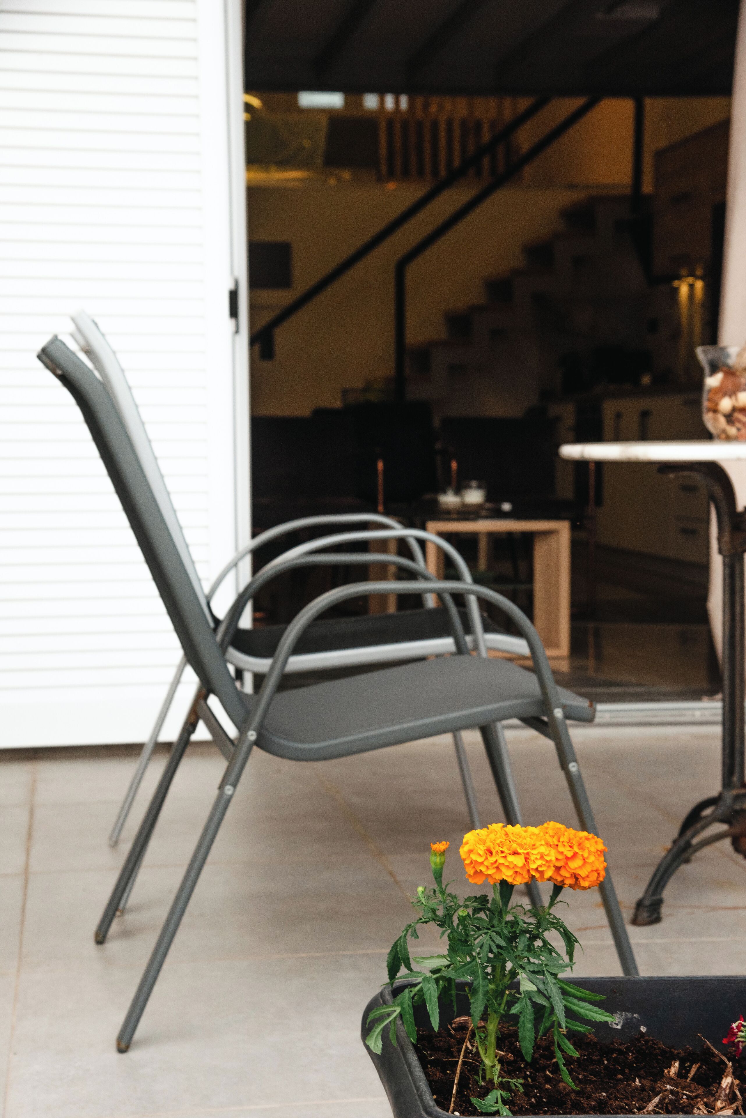 Una silla con estructura metálica y una planta en maceta con flores anaranjadas.