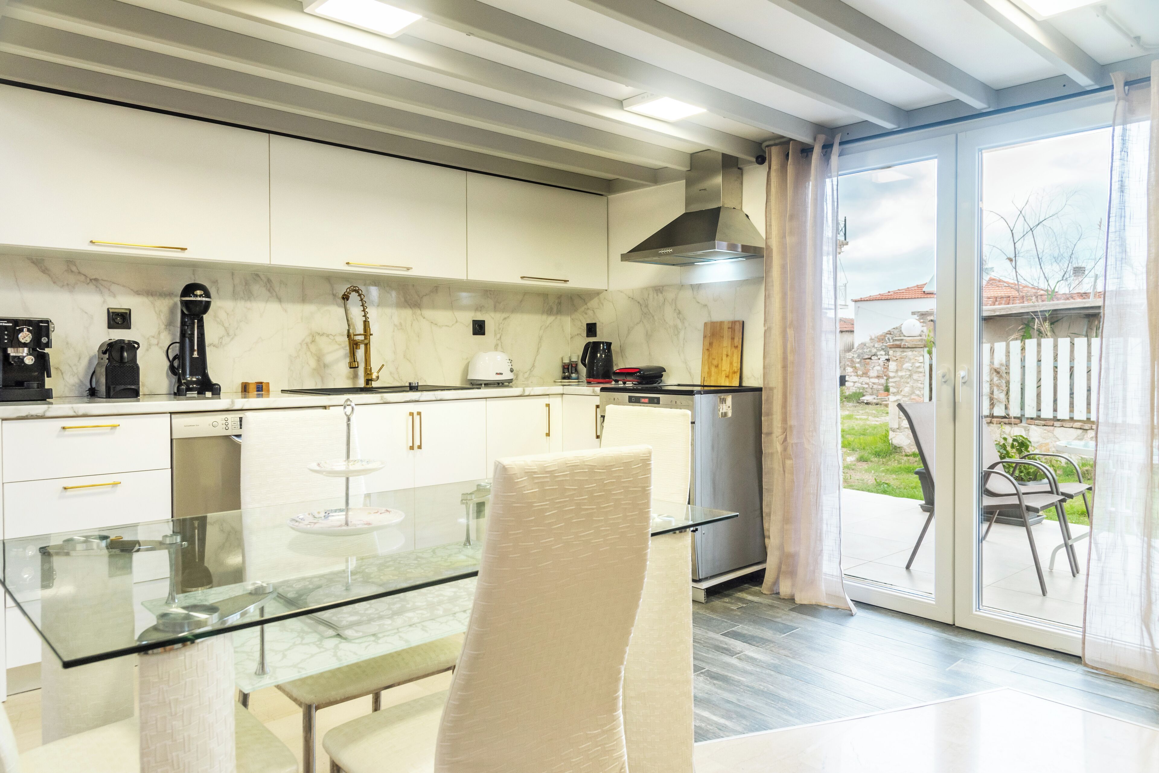 A modern kitchen with white cabinets, a glass dining table, and a sliding glass door leading to a patio.
