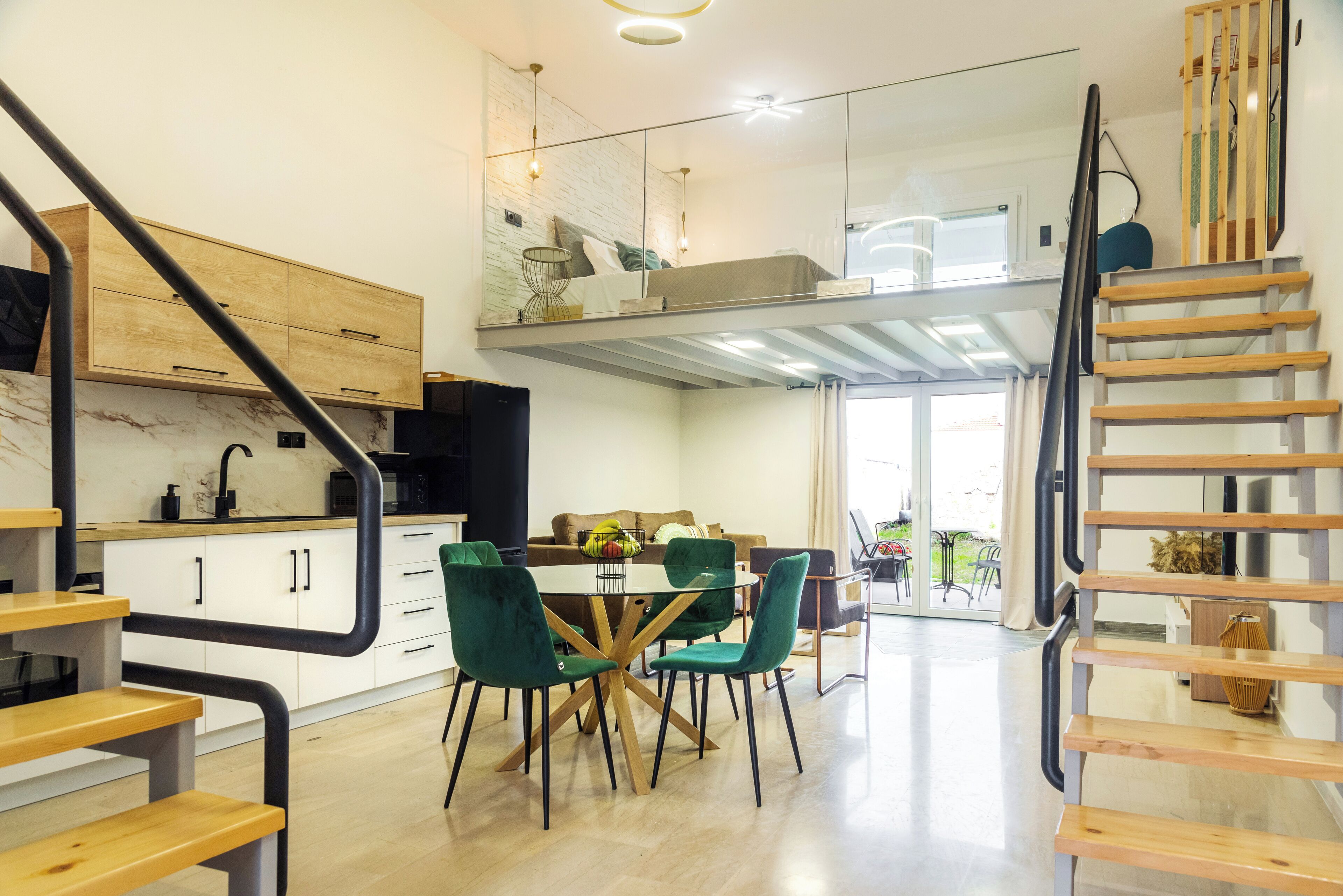 Une cuisine moderne avec un coin repas, un escalier en bois et une chambre en mezzanine avec balcon.