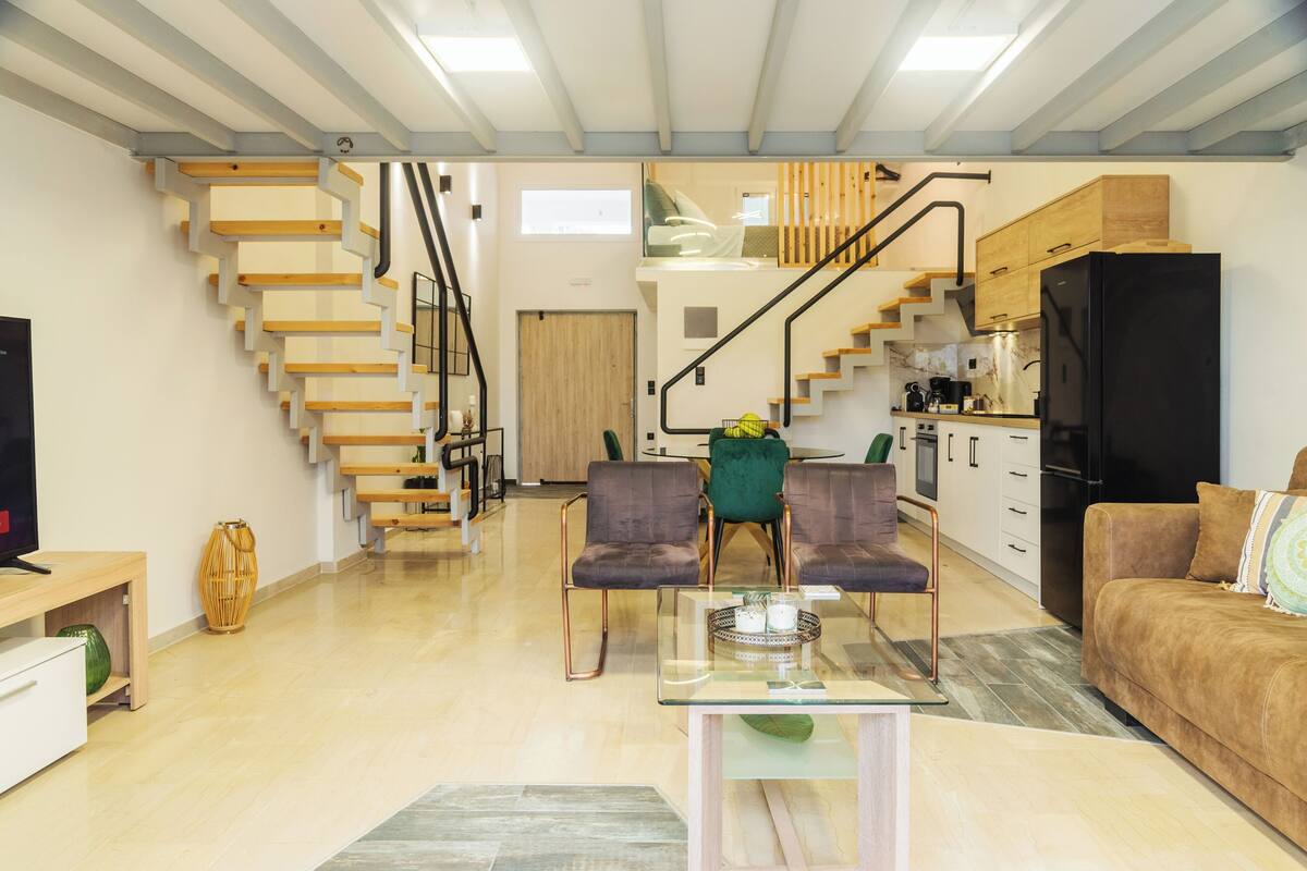 A modern living space with a staircase, kitchen, and seating area.