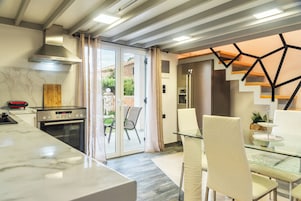 Una cocina moderna con encimera de mármol, electrodomésticos de acero inoxidable y una mesa de comedor de cristal con sillas.