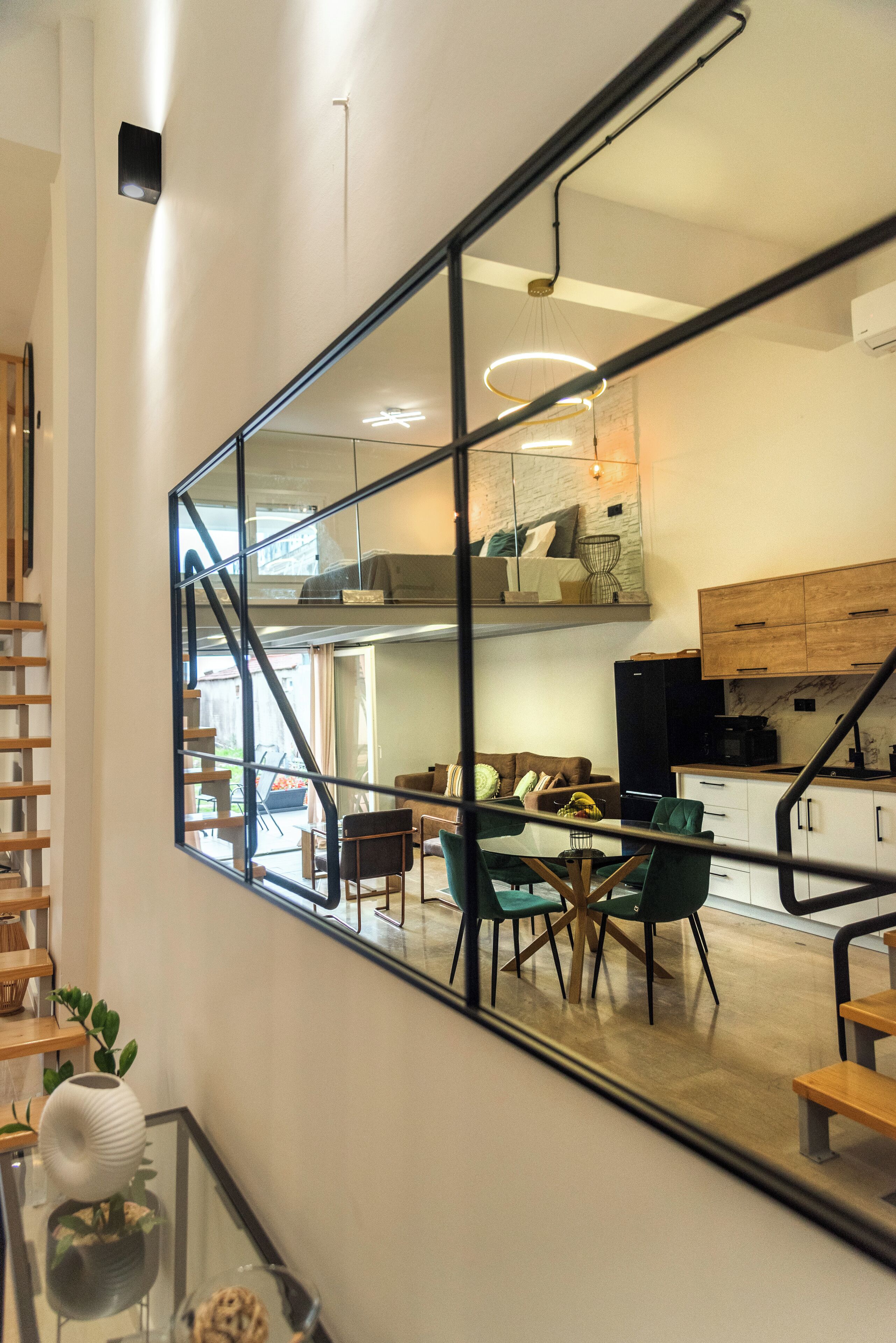 Una cocina moderna con armarios de madera, un comedor con mesa y sillas de vidrio, y una escalera con barandilla de metal.