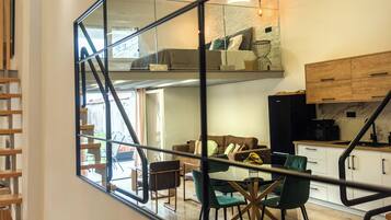 Una cocina moderna con armarios de madera, un comedor con mesa y sillas de vidrio, y una escalera con barandilla de metal.