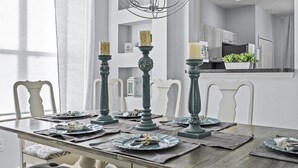 A dining table set with plates, napkins, and candles in a modern kitchen with white cabinetry and a hanging light fixture. - Ever After Adventure Villa (Kissimmee)