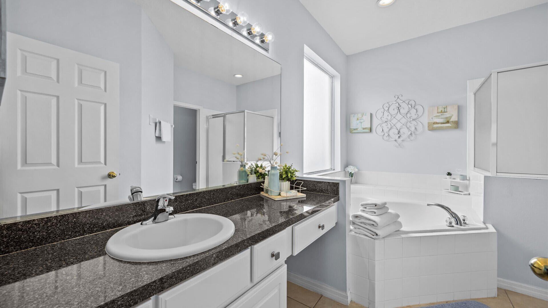 A modern bathroom with a granite countertop, a white sink, a large mirror, a bathtub, and a vanity with a mirror.
