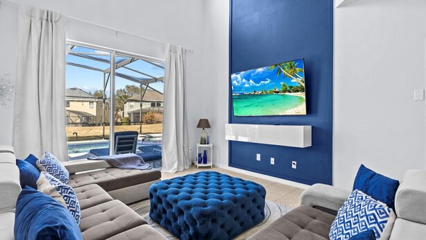 A living room with a pool view, a large TV on the wall, and a blue accent wall. - Ever After Adventure Villa (Kissimmee)
