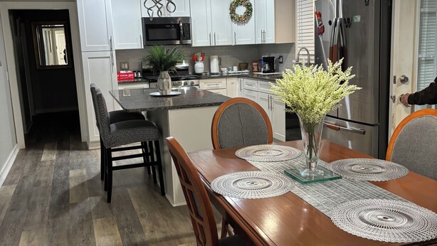 A modern kitchen with white cabinets, a stainless steel refrigerator, and a dining area with a wooden table and chairs. - BEAUTIFUL VACATION HOME          3 bedroom and 1 bathroom (Forest City)