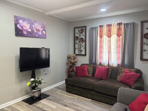 Una sala de estar con un televisor de pantalla plana, un sofá con cojines rojos, un florero con flores y un cuadro de flores en la pared.