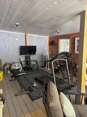 Zona de gimnasio con equipo de ejercicio, televisión e interior de madera.