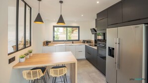 A modern kitchen with a large island, dark cabinets, stainless steel appliances, and pendant lighting.