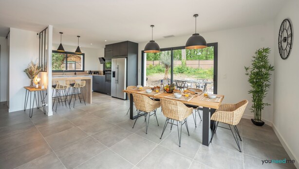 A modern kitchen with a dining area, large windows, and a clock on the wall.