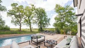 A deck with outdoor furniture, a pool, and trees in the background.