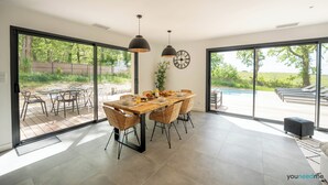 A spacious dining area with a large table and chairs, large windows, and a view of the outdoors.