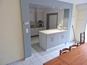 A modern kitchen with grey cabinets, a white countertop, and a dining area with a wooden table and chairs. - Maison 9 Personnes 800m de la Plage (Saint-Gilles-Croix-de-Vie)
