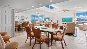 Un salon spacieux avec une grande table à manger, des sièges confortables et une vue sur l’océan par les fenêtres.