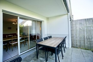 A patio with a dining table and chairs, a sliding glass door leading to an interior space, and a wooden fence.