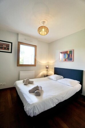 A hotel room with a bed, a bedside lamp, a window, and a painting on the wall.