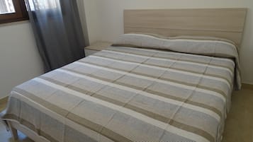 Un dormitorio con cama, mesita de noche y ventana con cortinas.