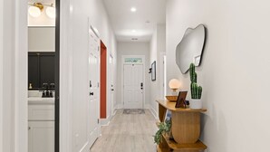 A hallway with white walls, a wooden floor, a mirror, a cactus, and a small wooden table with a lamp. - Charleston-themed House for 10! (Goose Creek)