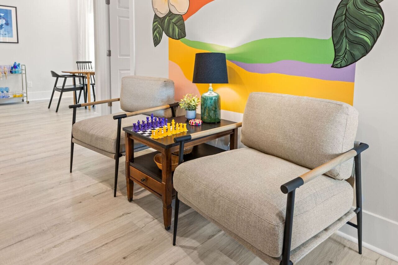Una habitación con un sofá, una mesa de madera con un juego de ajedrez, una lámpara y un mural colorido en la pared.