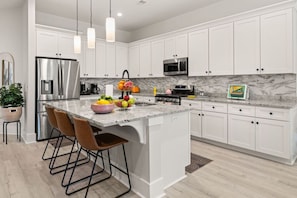 A modern kitchen with white cabinets, stainless steel appliances, and a marble countertop.
