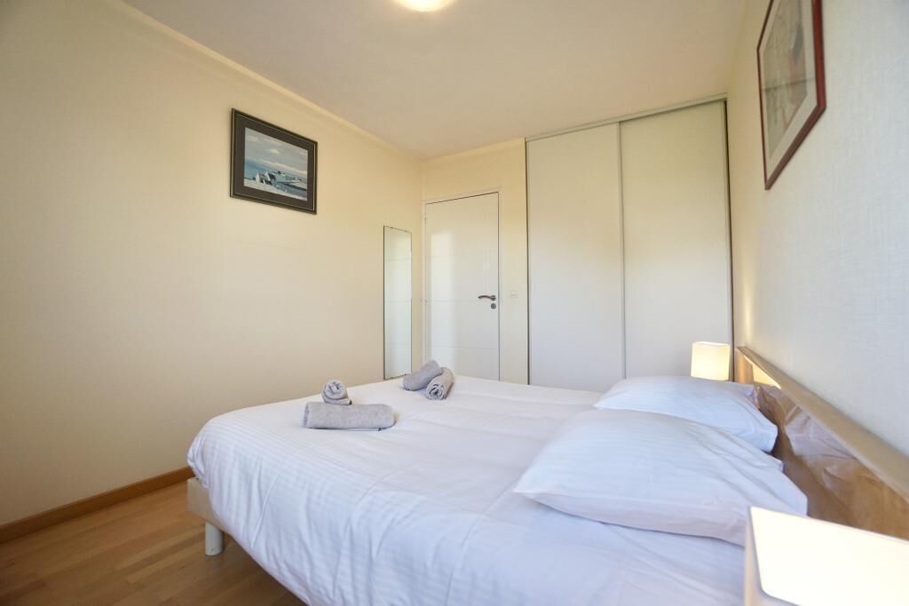 Une chambre d’hôtel avec un lit, une table de chevet avec une lampe, une porte et un tableau encadré au mur.