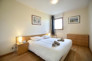 A hotel room with a bed, bedside tables, a nightstand, a dresser, and two framed pictures on the walls.
