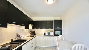 Een kleine keuken met witte kastjes, een zwart aanrecht, een magnetron en een spoelbak.